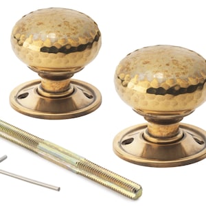 May include: Two antique brass door knobs with a hammered texture, each with a round base. A long threaded rod and an Allen key are included. The knobs have a vintage, rustic aesthetic, suitable for home decor and restoration projects.