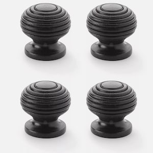 May include: Four black cabinet knobs with a round, grooved design. Each knob has a spherical top and a flared base, suitable for drawers or doors. The knobs are made of a solid, dark material.