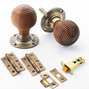 May include: A selection of door hardware in an antique style. The image shows two wooden doorknobs with brass bases, brass hinges, and a door latch. The doorknobs have a grooved, spherical design. The hardware has a warm, antique brass finish.
