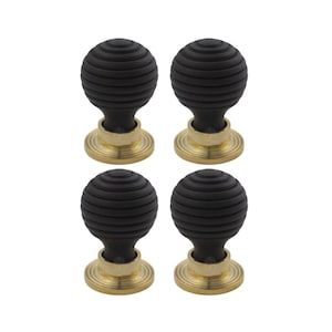May include: Four black, ribbed cabinet knobs with brass-coloured bases. The knobs have a spherical shape with horizontal grooves, and the bases are circular with a ridged design. The knobs are set against a white background.