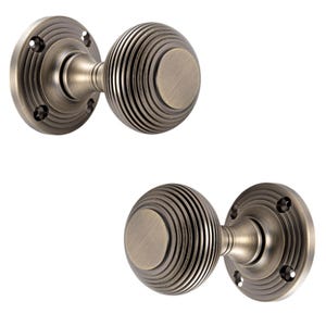 May include: Two antique bronze door knobs with a ribbed, spherical design. Each knob has a circular backplate with screw holes. The knobs are set against a white background.