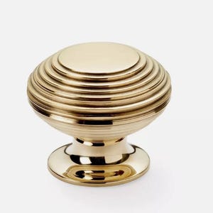 May include: A gold cabinet knob with a distinctive ridged design. The knob features a smooth, rounded top and a circular base. The metal hardware is suitable for furniture or cabinetry. The knob's dimensions are in centimetres.