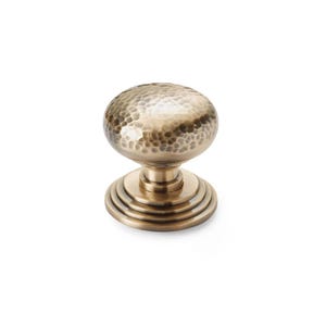 May include: A bronze cabinet knob with a hammered texture on the round top. The knob sits on a base with concentric circular ridges. This hardware is suitable for drawers, cabinets, and furniture.