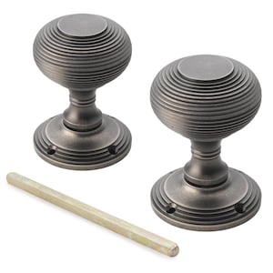 May include: Two antique-style door knobs with a grooved, spherical design. The knobs are a dark, muted metallic colour, with a matching base and a metal rod. The hardware is designed for doors and cabinets.