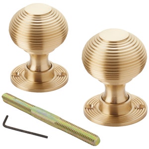 May include: Two brass door knobs with a ribbed, spherical design. Each knob sits on a circular base. A threaded rod and an Allen key are included. The knobs are a warm, golden colour.