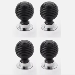 May include: Four black, round cabinet knobs with a grooved design. Each knob sits on a silver-coloured base. The knobs are evenly spaced against a white background, offering a clean and modern aesthetic.