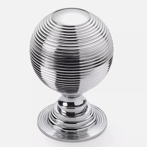 May include: A polished chrome decorative knob with a spherical top featuring concentric ridges. The knob sits on a tiered base with a circular foot. The design is modern and minimalist, suitable for furniture or cabinetry.