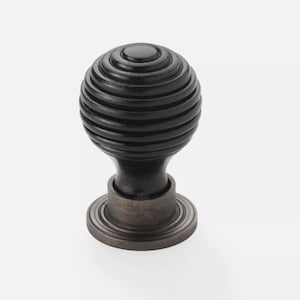 May include: A black, spherical cabinet knob with a grooved design. The knob sits atop a dark, cylindrical base with a circular, ridged plate. This decorative hardware is suitable for drawers and cabinets.