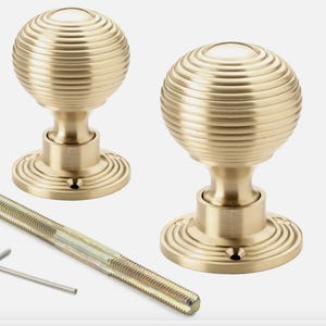 May include: Two brass door knobs with a ribbed, spherical design. The knobs sit on a circular base with a decorative edge. A threaded rod and an Allen key are also included.