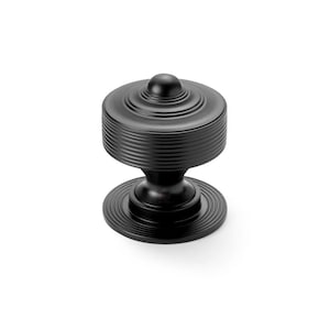 May include: A black cabinet knob with a round, ridged top and base, connected by a smaller, cylindrical stem. The knob has a small, rounded top and is set against a white background.