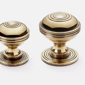 May include: Two brass door knobs with a classic design. The knobs have a round, ridged top and a circular base. The brass has a polished finish. These knobs are likely for interior doors.