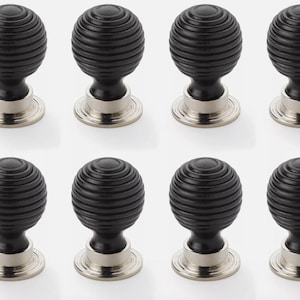 May include: Eight black cabinet knobs with a ribbed, spherical design. Each knob has a silver-coloured base. These decorative knobs are suitable for drawers, cabinets, or furniture.