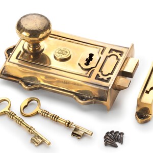 May include: A brass door lock set with a hammered knob, two skeleton keys, and a strike plate. The lock features an ornate design and includes mounting screws. The set is made of polished brass.