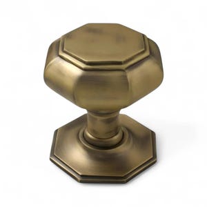 May include: Antique brass door knob with an octagonal design. The knob has a classic, vintage aesthetic, with a warm, metallic finish. The base and the top of the knob are also octagonal, creating a cohesive and symmetrical look.