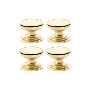 May include: Four gold cabinet knobs. Each knob features a rounded top, a cylindrical base, and a circular mounting plate. The knobs are made of a shiny, reflective material, and are arranged in a square formation against a white background.