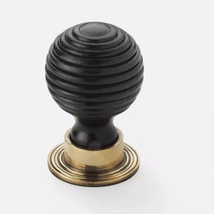 May include: A black, spherical cabinet knob with a grooved design. The knob sits on a brass-coloured base with concentric circles. This decorative hardware is suitable for drawers and cabinets.