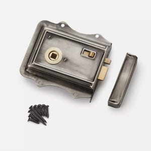 May include: A distressed silver door lock with brass-coloured details, including the keyhole and latch. The set includes a separate strike plate and a small collection of black screws. A classic, vintage design.