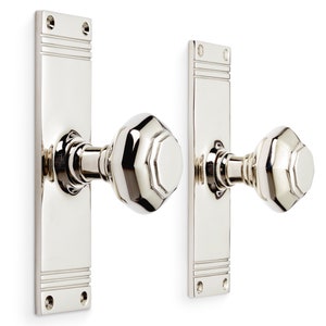 May include: Two polished nickel door handles. Each handle features a rectangular backplate with decorative horizontal lines and a faceted, geometric knob. The hardware is designed for interior doors, adding a touch of elegance.