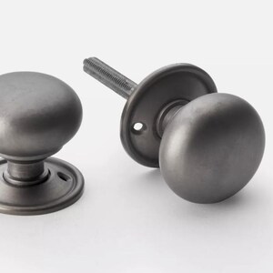 May include: Two dark grey antique door knobs. One is assembled with a backplate and threaded rod, the other is a standalone knob. The knobs have a rounded shape and a classic design, suitable for interior doors.