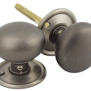 May include: A pair of antique-style door knobs in a dark grey finish. The knobs are spherical and have a slightly textured surface. Each knob is mounted on a circular backplate. The set includes a threaded rod for fitting.