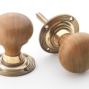 May include: Two wooden door knobs with brass fittings. The knobs are light brown and spherical. The brass fittings include a circular base with concentric grooves and a threaded rod for installation. The knobs are a classic design.