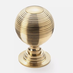 May include: A gold-coloured, spherical cabinet knob with a ridged design. The knob sits on a short, tiered base, also in gold. The design is symmetrical and decorative, suitable for furniture or cabinetry.