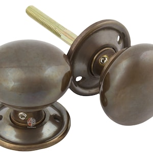 May include: A pair of bronze-coloured door knobs with a traditional, rounded shape. Each knob has a smooth, polished finish and is attached to a circular backplate. The set includes a threaded spindle for fitting. Suitable for interior doors.