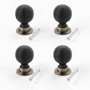 May include: Four black cabinet knobs with a ribbed, spherical design. Each knob has a bronze-coloured base and comes with a silver screw for installation. The knobs are arranged on a white surface.