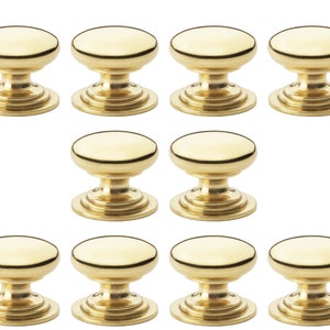 May include: Ten gold-coloured cabinet knobs are displayed. Each knob features a rounded top and a decorative base. These metal knobs are designed for drawers or cabinet doors. The knobs are presented against a white backdrop.