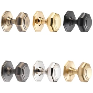 May include: A selection of six octagonal door knobs in finishes including antique brass, polished brass, matte black, pewter, polished nickel, and satin brass. Each knob has a matching backplate and a classic, geometric design.