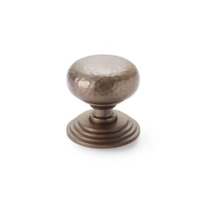 May include: A bronze cabinet knob with a hammered texture on the rounded top. The knob sits on a tiered base, creating a classic, decorative hardware piece. Suitable for adding elegance to furniture.