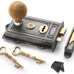 May include: A cast iron door lock set with a wooden knob, brass details, and two ornate keys. The set includes a strike plate and screws. The lock has a decorative design and a circular emblem.