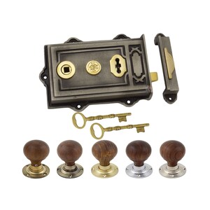 May include: A traditional door lock set featuring a dark grey metal lock with brass details and two keys. The set includes a rectangular lock, a latch, and five wooden doorknobs with brass and silver-toned bases. The doorknobs are round.