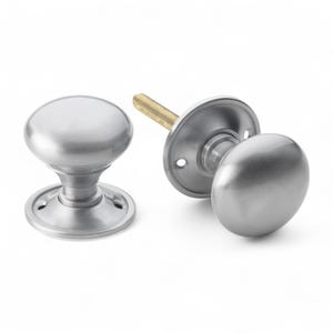 May include: Two brushed nickel door knobs. One is assembled, showing the round knob, base, and threaded rod. The other is separate, showing the round knob and base. The knobs have a smooth, matte finish. Suitable for interior doors.