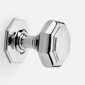 May include: A shiny chrome door knob, featuring an octagonal backplate and handle. The door furniture has a reflective surface and is set against a white backdrop. This is a classic style door knob, suitable for various interior designs.