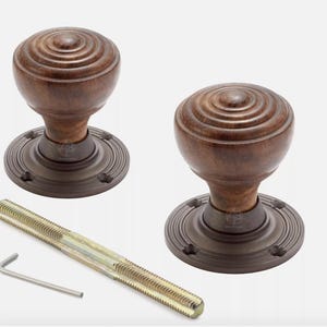 May include: Two brown wooden door knobs with a circular design, set on a bronze-coloured base. A long threaded rod and an Allen key are included. The door knobs are a classic design.