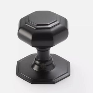 May include: A black, octagonal door knob with a matching base. The knob has a geometric design and a matte finish. The door knob is made of metal and is likely for a front door or interior door.
