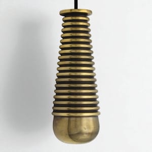 May include: A brass-coloured, cylindrical pendant light fitting with a series of stacked, rounded rings. The fitting has a rounded top and a bulbous bottom. A black cord suspends the light against a white background.