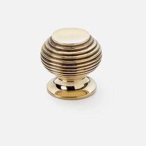 May include: A brass cabinet knob with a spherical design. The knob has horizontal ridges, creating a textured surface. The base is circular and polished, reflecting light. Suitable for furniture and home decor.