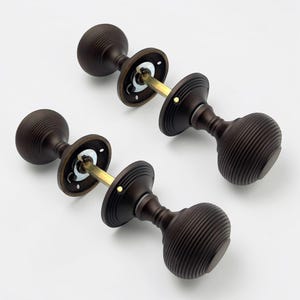 May include: Four antique bronze door knobs with a ribbed, spherical design. Each knob has a circular backplate and a brass-coloured connecting rod. The knobs are arranged on a white background, showcasing their classic hardware style.