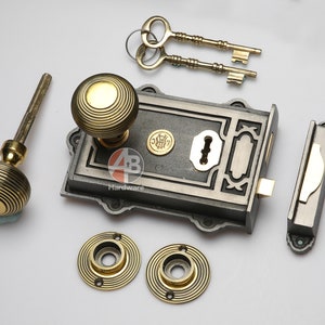 May include: An antique door hardware set, including a lock, two keys, two doorknob roses, and a door handle. The set has a dark grey finish with brass accents. The doorknobs and roses have a grooved design.