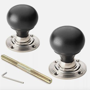 May include: Two black door knobs with a round shape and a silver base. The knobs are accompanied by a long screw and an Allen key. The door knobs have a classic design.