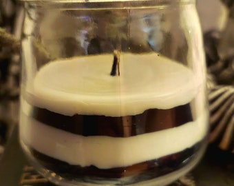 Könnte beinhalten: Ein klares Glas-Kerzengefäß mit goldenem Deckel. Die Kerze ist in Schichten aus weißem und schwarzem Wachs geschichtet.