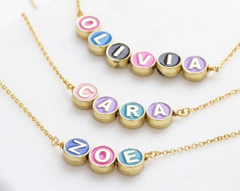 May include: Three gold necklaces with colorful letter beads spelling out the names Olivia, Cara, and Zoe.
