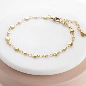 Peut inclure: Un bracelet en or avec des breloques en forme de cœur et une chaîne délicate. Le bracelet est doté d'un fermoir à ressort et d'une chaîne d'extension réglable.