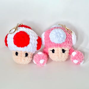 May include: Two crocheted mushroom keychains, one red and white, the other pink and white.