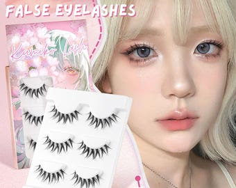 Könnte beinhalten: Drei Paar schwarze Kunstwimpern werden präsentiert. Die Verpackung trägt die Aufschrift "3 Pairs False Eyelashes" und zeigt den Markennamen "Kumiko Lash" mit einer Illustration im Anime-Stil. Im Hintergrund ist eine Person mit heller Haut und blauen Augen zu sehen.