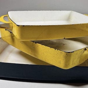 Puede incluir: Una taza de cerámica blanca con asa negra y el texto "But First, Coffee" en negrita negra. La taza se encuentra sobre un fondo borroso, sugiriendo un ambiente acogedor.