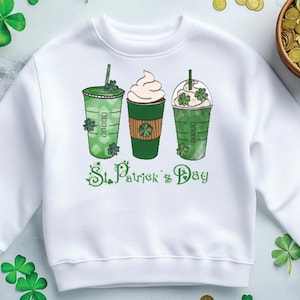 May include: White sweatshirt featuring three green St. Patrick's Day themed drinks with shamrock accents. The words "St. Patrick's Day" are written in green script below the drinks. Green shamrocks and gold coins are scattered around the sweatshirt.