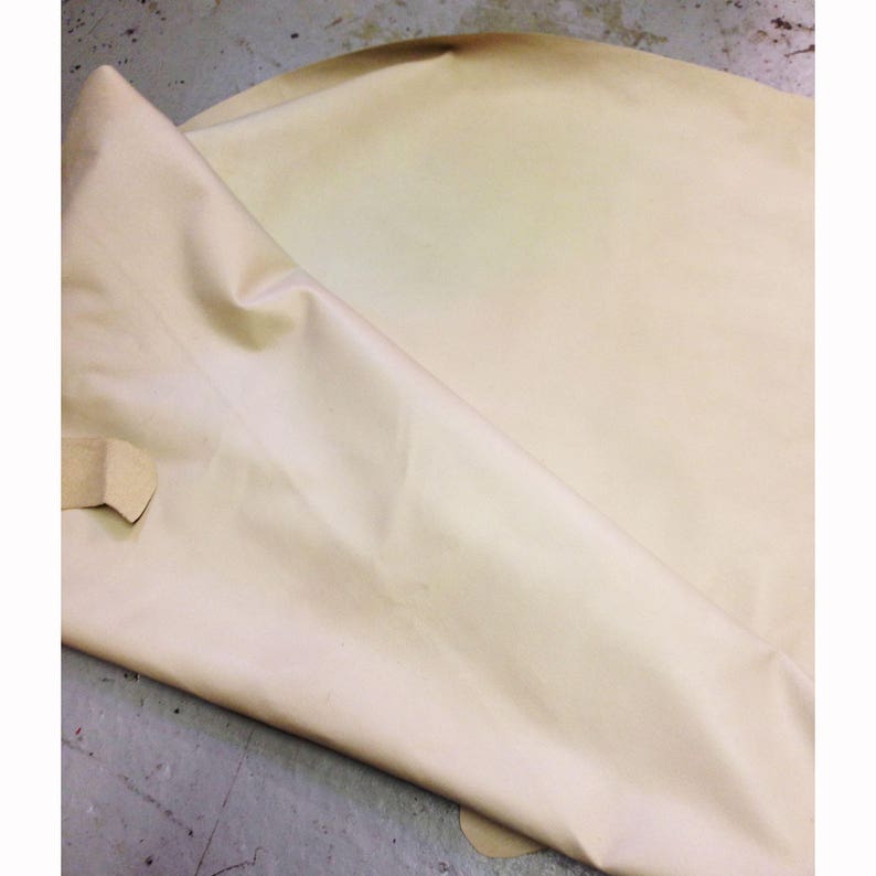 May include: A large sheet of light beige leather, folded over to reveal its underside. The leather has a smooth texture and a slight sheen. The material appears supple and ready for crafting, with a few small imperfections.
